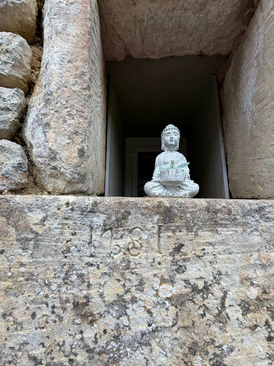 Bouddha posé dans une niche de la longère de l'Éco-Hameau SOI, au-dessus de la pierre gravée de 1681