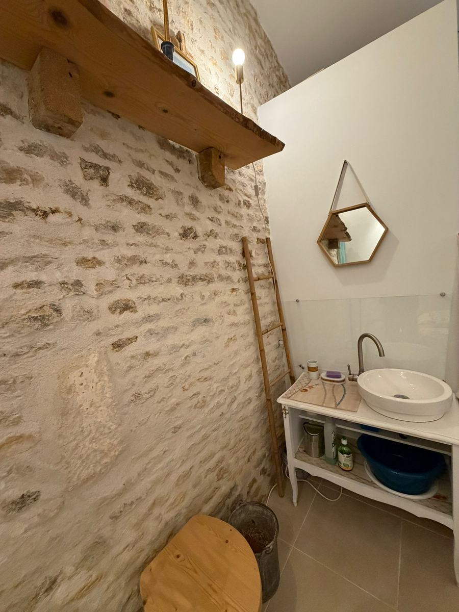 Coin salle d'eau du Studio Zen : lavabo, miroir hexagonal et toilettes sèches contre le mur en pierre